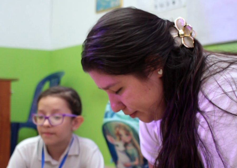 Profesora acompañando a una estudiante durante una actividad en el salón